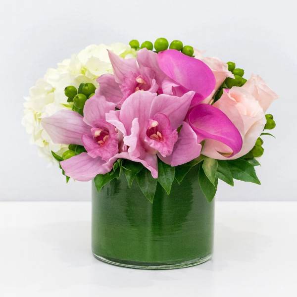 Pink orchids and pale roses arranged in a green glass vase