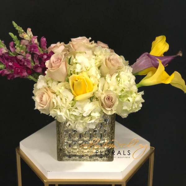 Bouquet of pale roses, white hydrangeas, and yellow calla lilies in a textured vase.