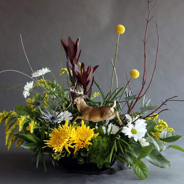 Mixed floral arrangement with a deer figurine in a low black container