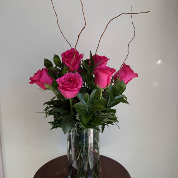 Pink roses arranged in a clear glass vase with tall curly branches