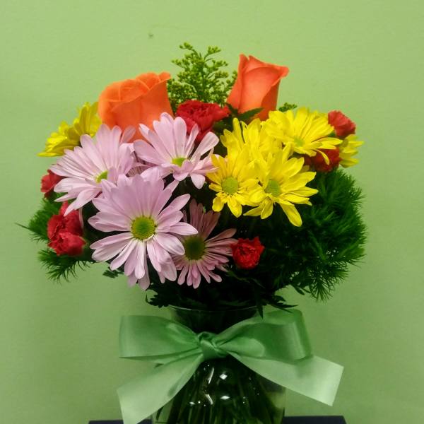 Bouquet of orange roses, daisies, and red carnations in a glass vase with a ribbon