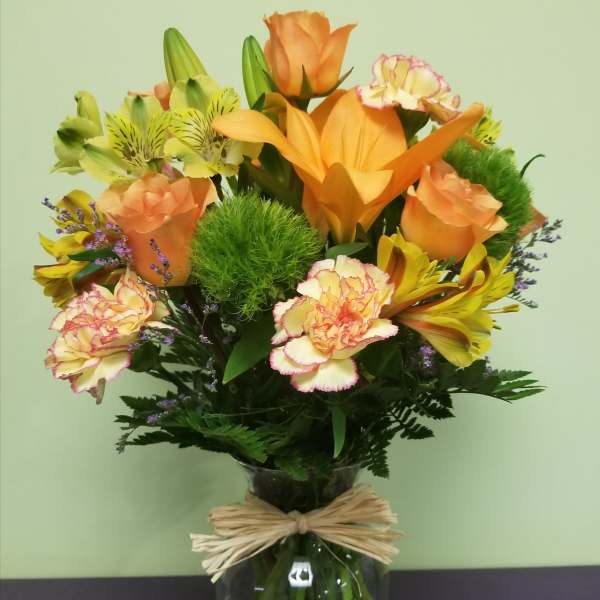 Orange and yellow mixed bouquet in a glass vase with a raffia bow