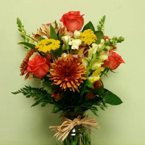 Mixed bouquet of orange roses, yellow blooms, and chrysanthemums in a glass vase