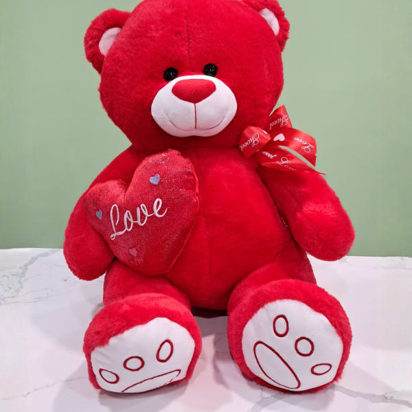 Red teddy bear holding a heart with a ribbon