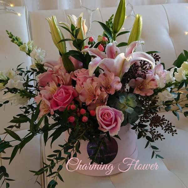 Pink lilies and roses arranged in a pale hatbox with greenery