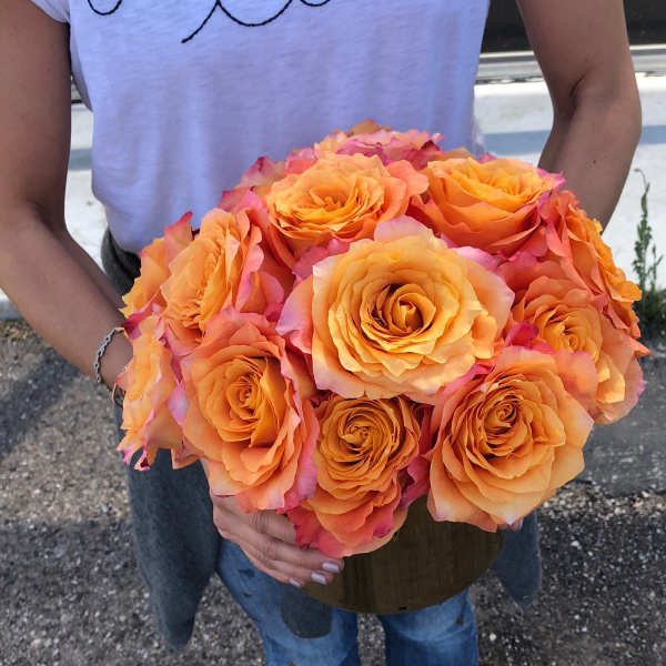 Person holding a bouquet of orange roses in a vase