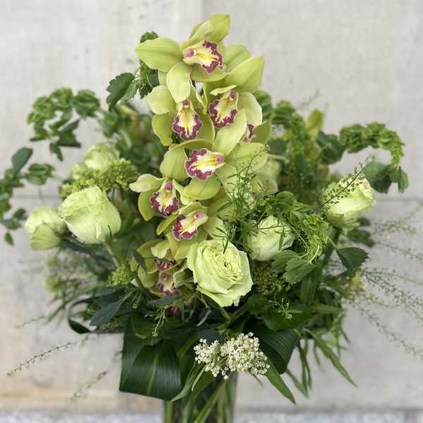 Tall green orchid arrangement in a glass vase with mixed foliage