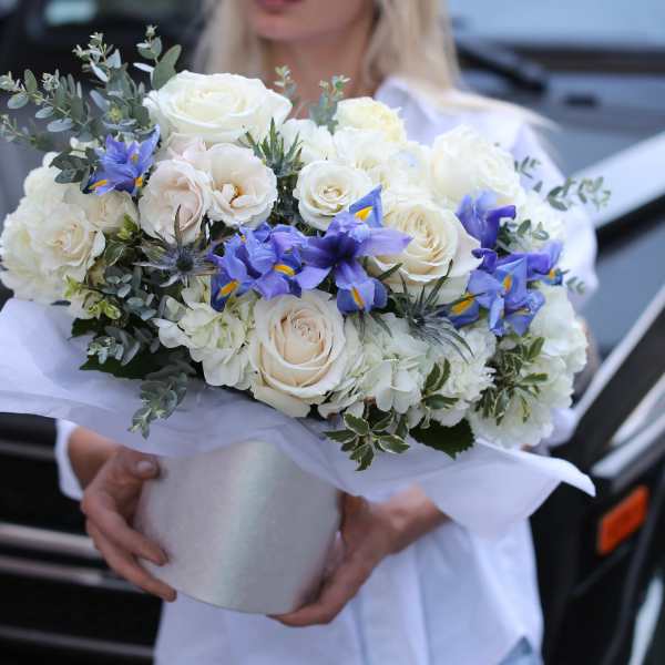 Bouquet of white roses and blue irises wrapped in white paper