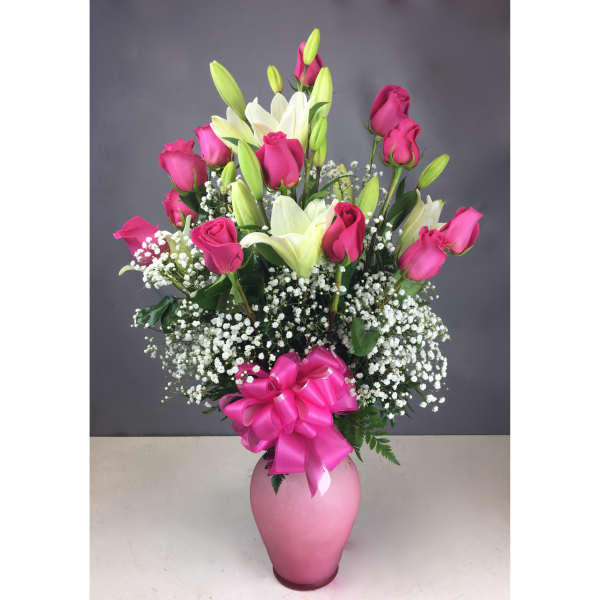 Pink roses and white lilies in a pink vase with a ribbon