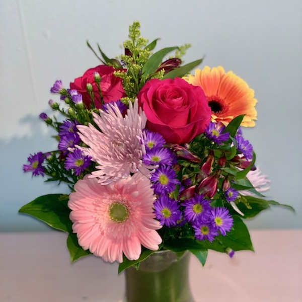 Mixed bouquet of pink roses, gerbera daisies, and purple daisies in a glass vase