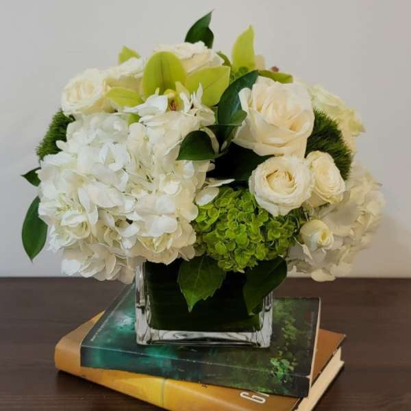 White and green floral arrangement in a square glass vase