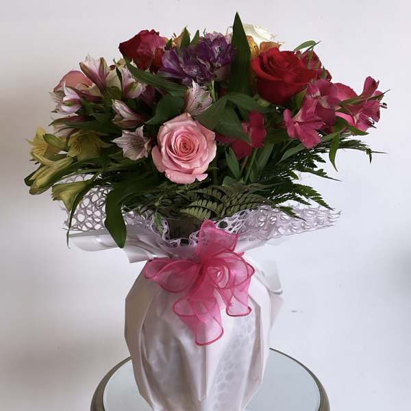 Mixed bouquet of roses and alstroemeria in a wrapped vase with a pink ribbon