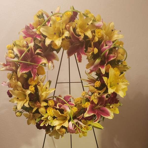 Large floral wreath on a black stand with yellow lilies and pink flowers
