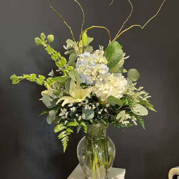 Tall white and pale blue floral arrangement in a glass vase