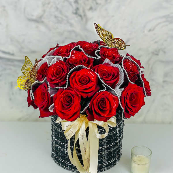 Red roses arranged in a black round box with a cream ribbon