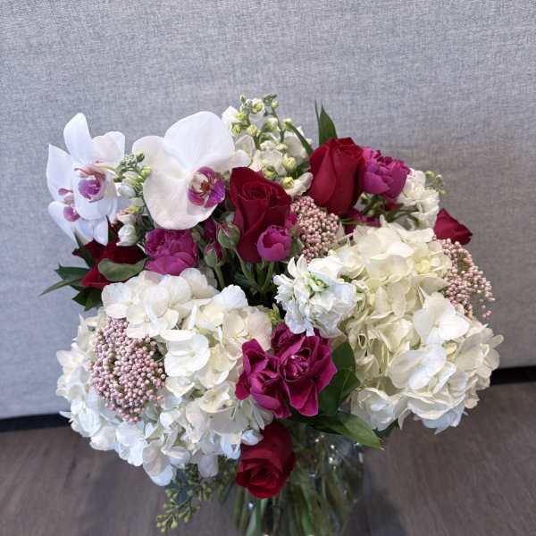 Bouquet of red roses, white orchids, and white hydrangeas in a glass vase