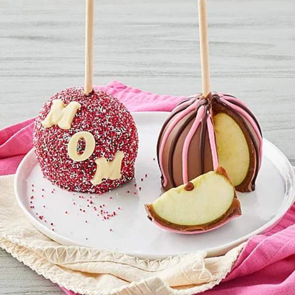Two chocolate-covered caramel apples on sticks, one with sprinkles and letters