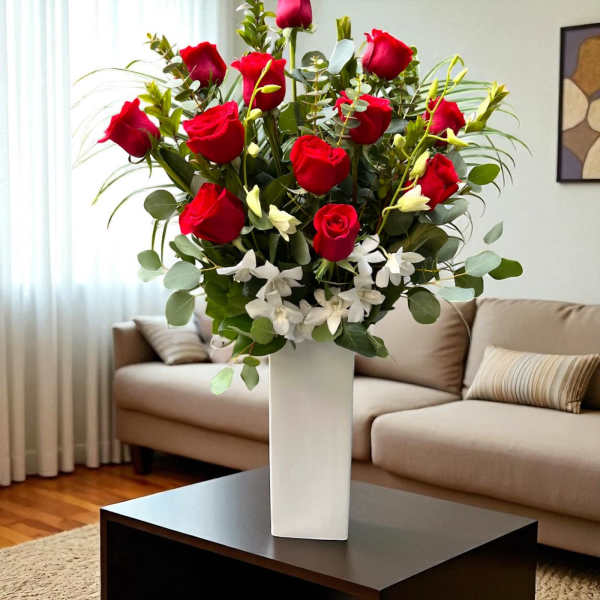 Tall arrangement of red roses and white flowers in a white rectangular vase on a coffee table