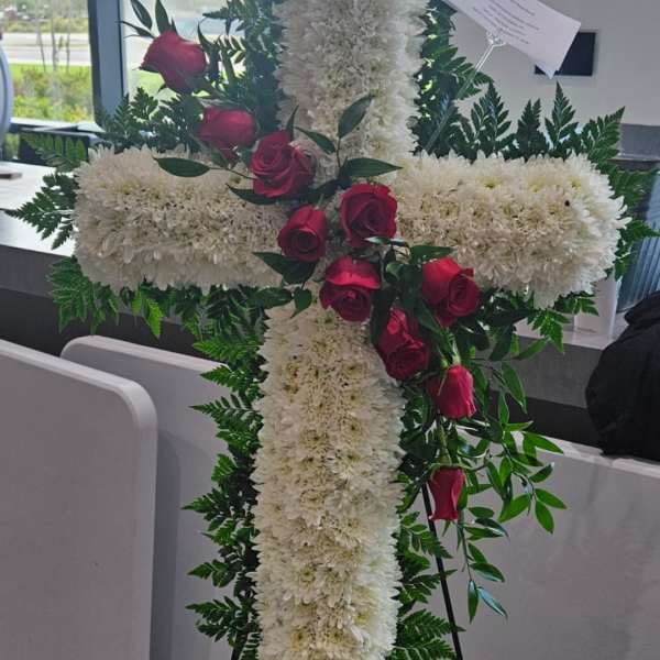 White floral cross on an easel with red roses