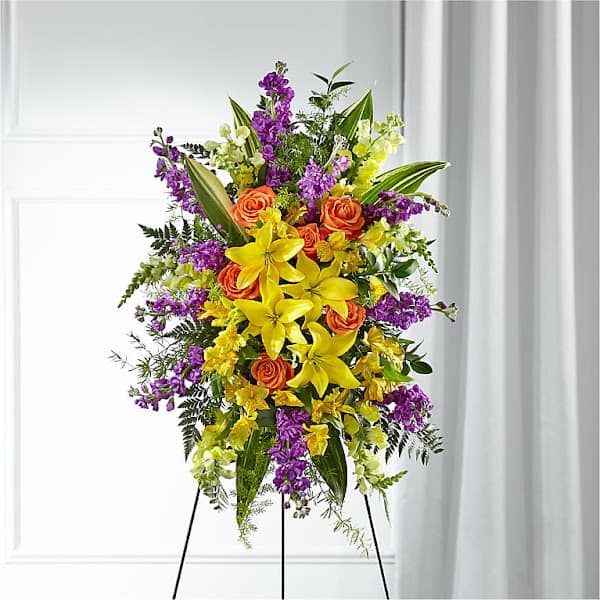 Standing floral spray with yellow lilies, orange roses, and purple flowers