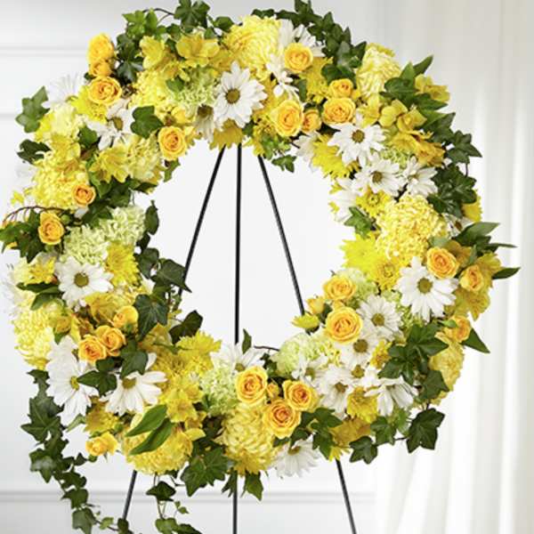 Large yellow and white floral wreath with ivy displayed on a metal easel stand