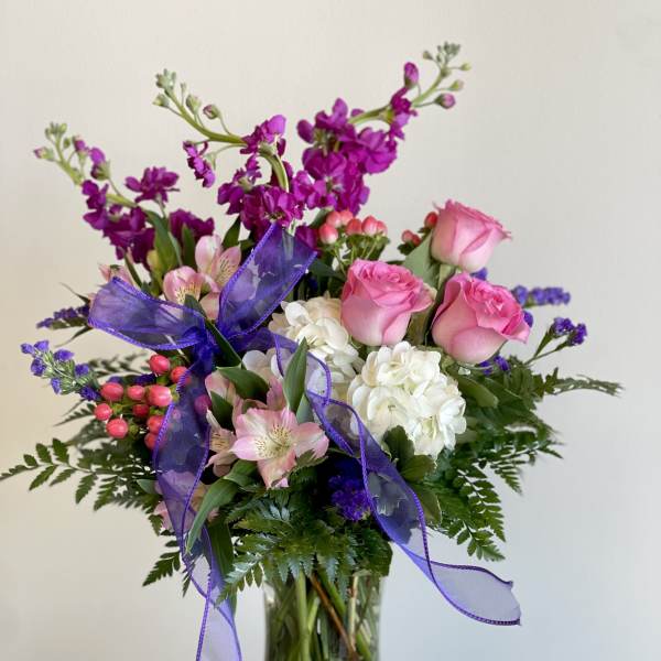 Pink roses and white hydrangeas in a glass vase with purple ribbon