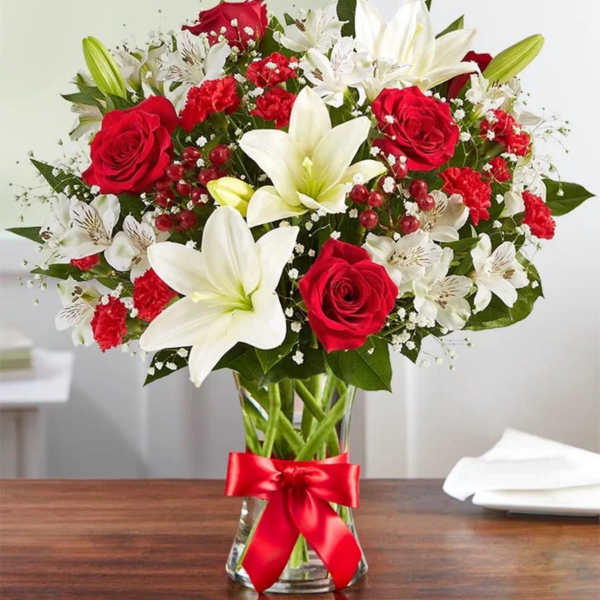 Red roses and white lilies in a clear glass vase with a red ribbon