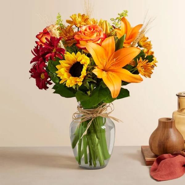 Bouquet of orange lilies, roses, sunflowers, and red daisies in a glass vase