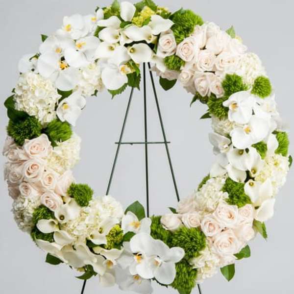 Large wreath of white orchids, calla lilies, hydrangeas and blush roses on a metal easel stand