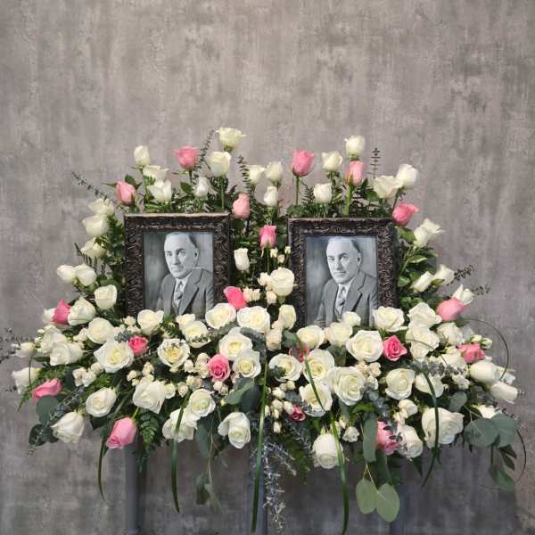 Symmetrical floral tribute with two framed portraits surrounded by white and pink roses