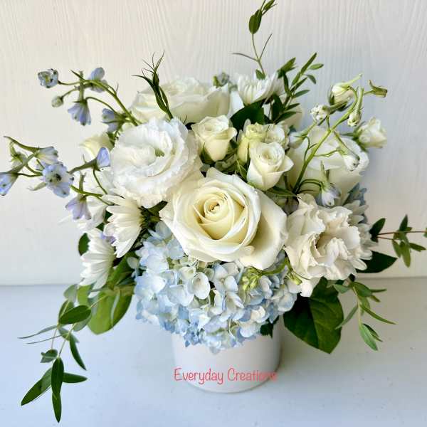 White roses and pale blue hydrangeas in a white vase