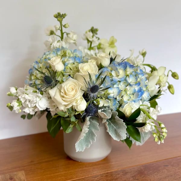 White roses and blue hydrangeas arranged in a white vase