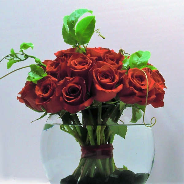 Compact bouquet of red roses in a round glass bowl with looping green vines