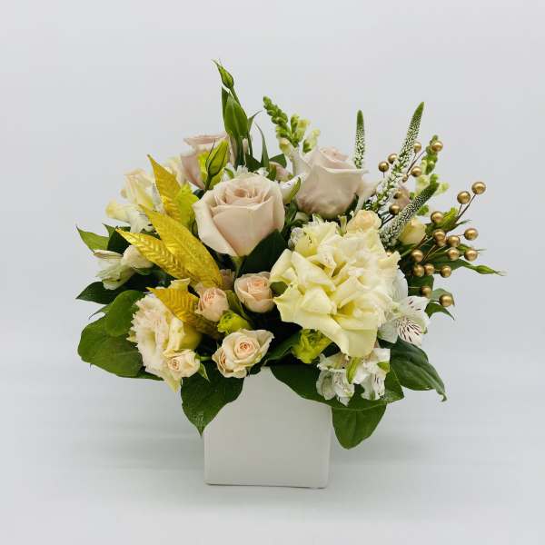 Low arrangement of cream roses and mixed white flowers in a square white vase