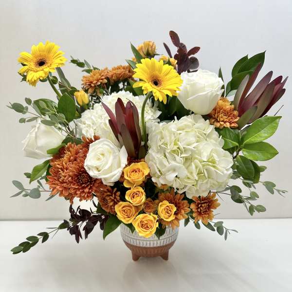 Mixed bouquet of white roses, hydrangeas, and yellow gerberas in a ceramic vase