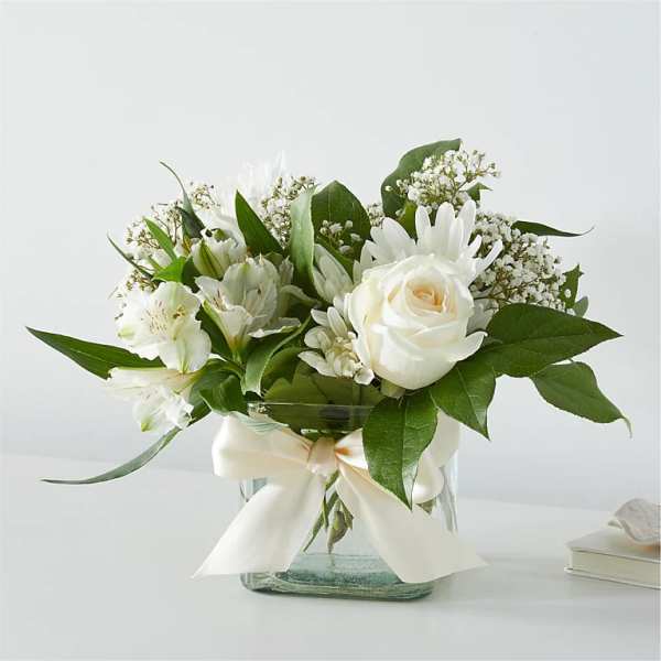 White roses and daisies arranged in a glass vase with a ribbon