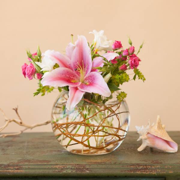 Pink lily and small pink roses in a round glass vase