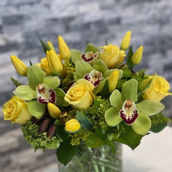 Yellow roses and orchids arranged in a glass vase