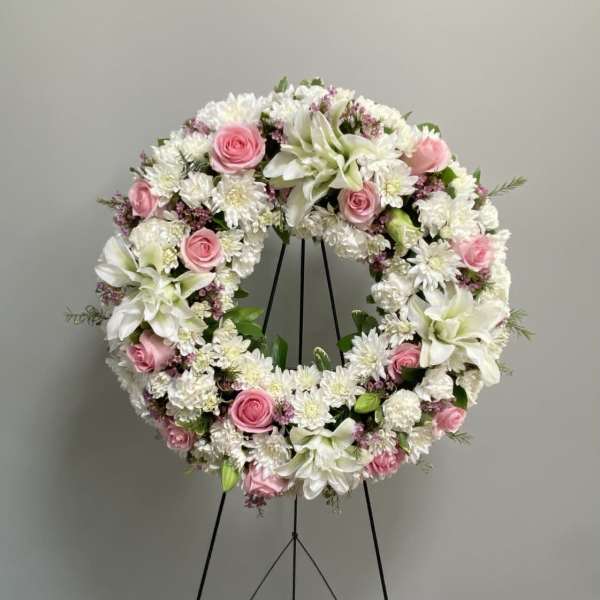 Circular floral wreath with pink roses and white blooms on a black stand