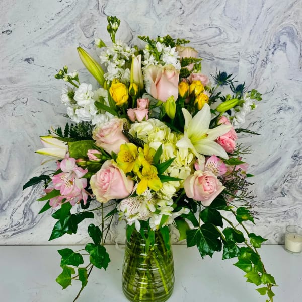 Mixed bouquet of pink roses, white lilies, and yellow flowers in a glass vase