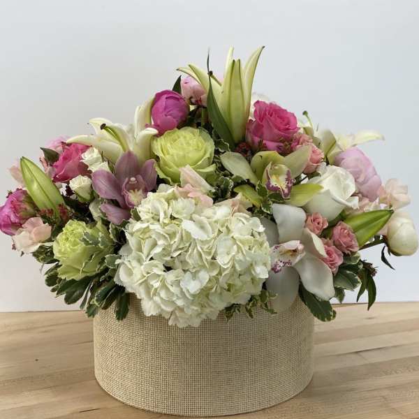 Mixed pink and white floral arrangement in a round beige box