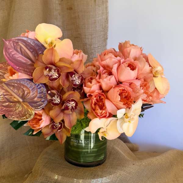 Peach roses and orchids arranged in a green glass vase