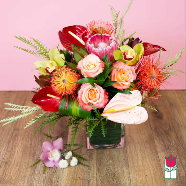 Mixed tropical bouquet in a square glass vase with pink and red blooms