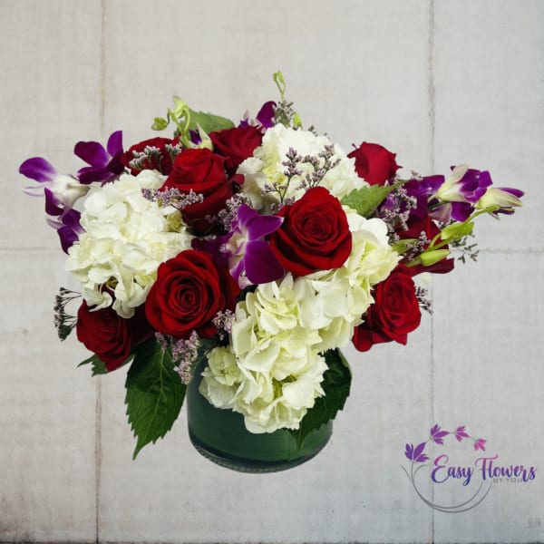 Red roses and white hydrangeas in a green glass vase with purple orchids