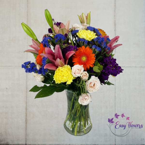Mixed bouquet in a clear glass vase with lilies, roses, and bright daisies