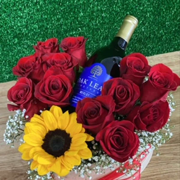 Red roses and a sunflower arranged around a wine bottle in a gift box