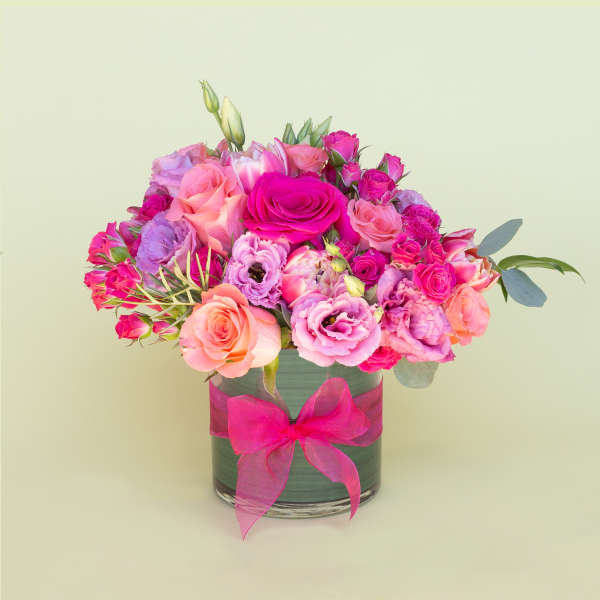 Pink and peach rose bouquet in a glass vase with a pink ribbon