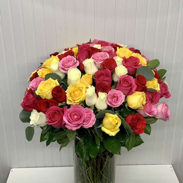 Tall vase of mixed red, pink, yellow, and white roses arranged in a full rounded display