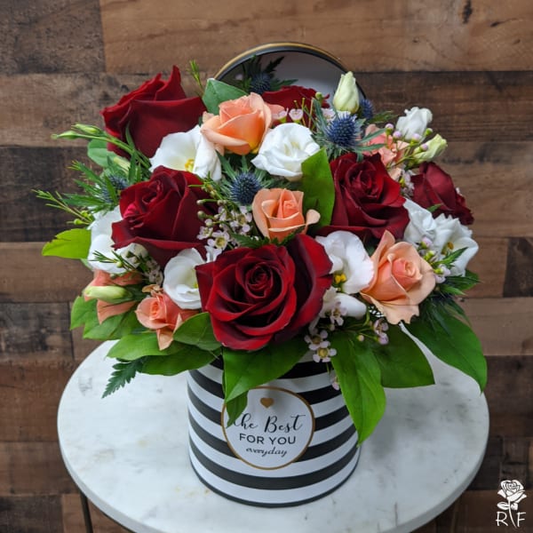 Bouquet of red, peach, and white roses in a striped hatbox