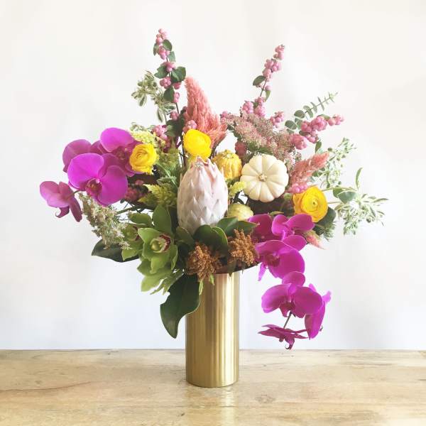 Mixed floral arrangement in a gold vase with pink orchids and yellow blooms